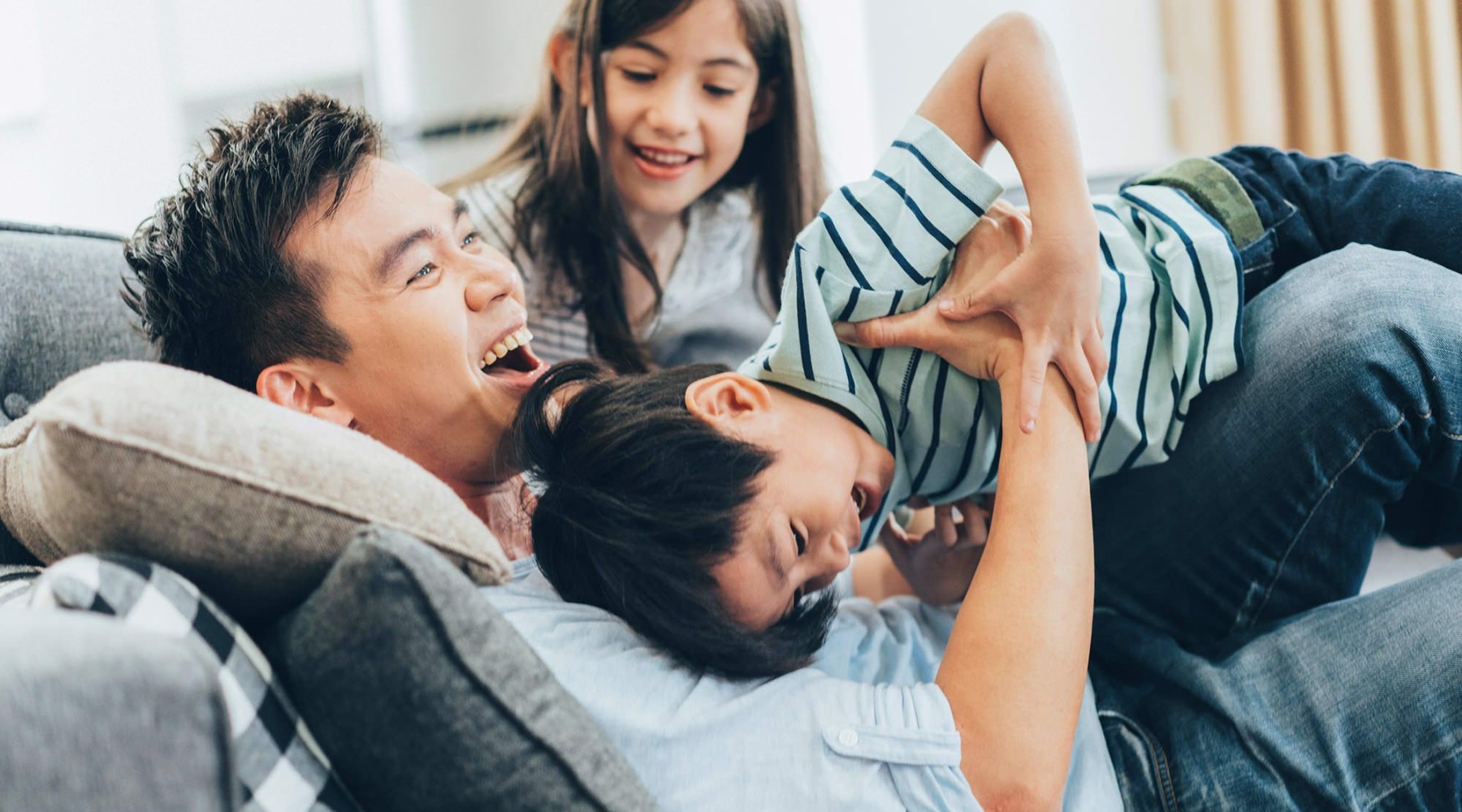 father plays on a couch with his young children